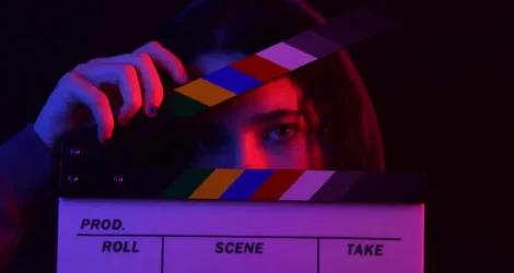 Person holding a film clapperboard under dramatic blue and red lighting, symbolizing video production, movie trailers, and digital entertainment.